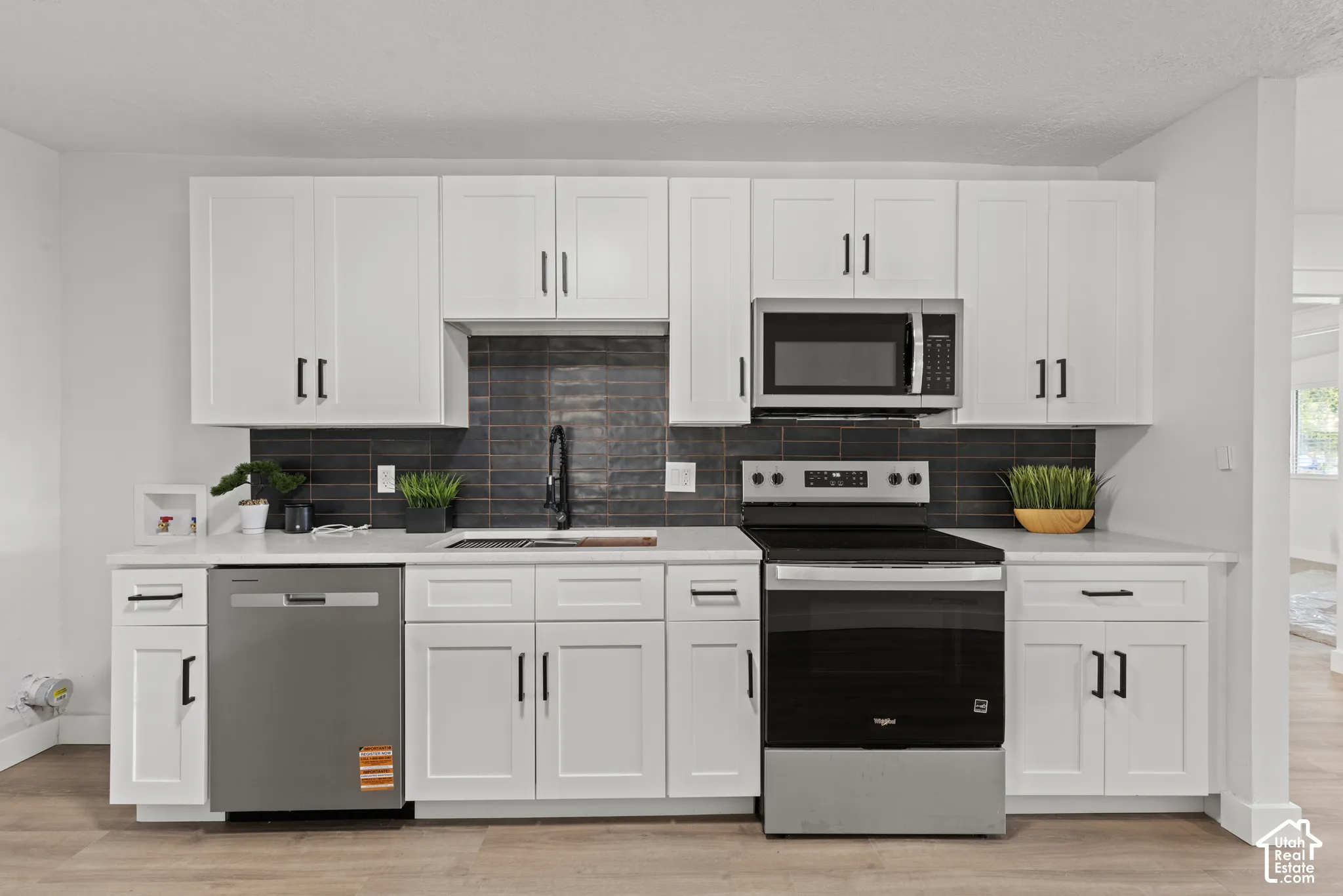 Kitchen featuring white shaker-style cabinetry, matte black hardware, stone-finish countertops, dark horizontal tile backsplash, and stainless steel appliances