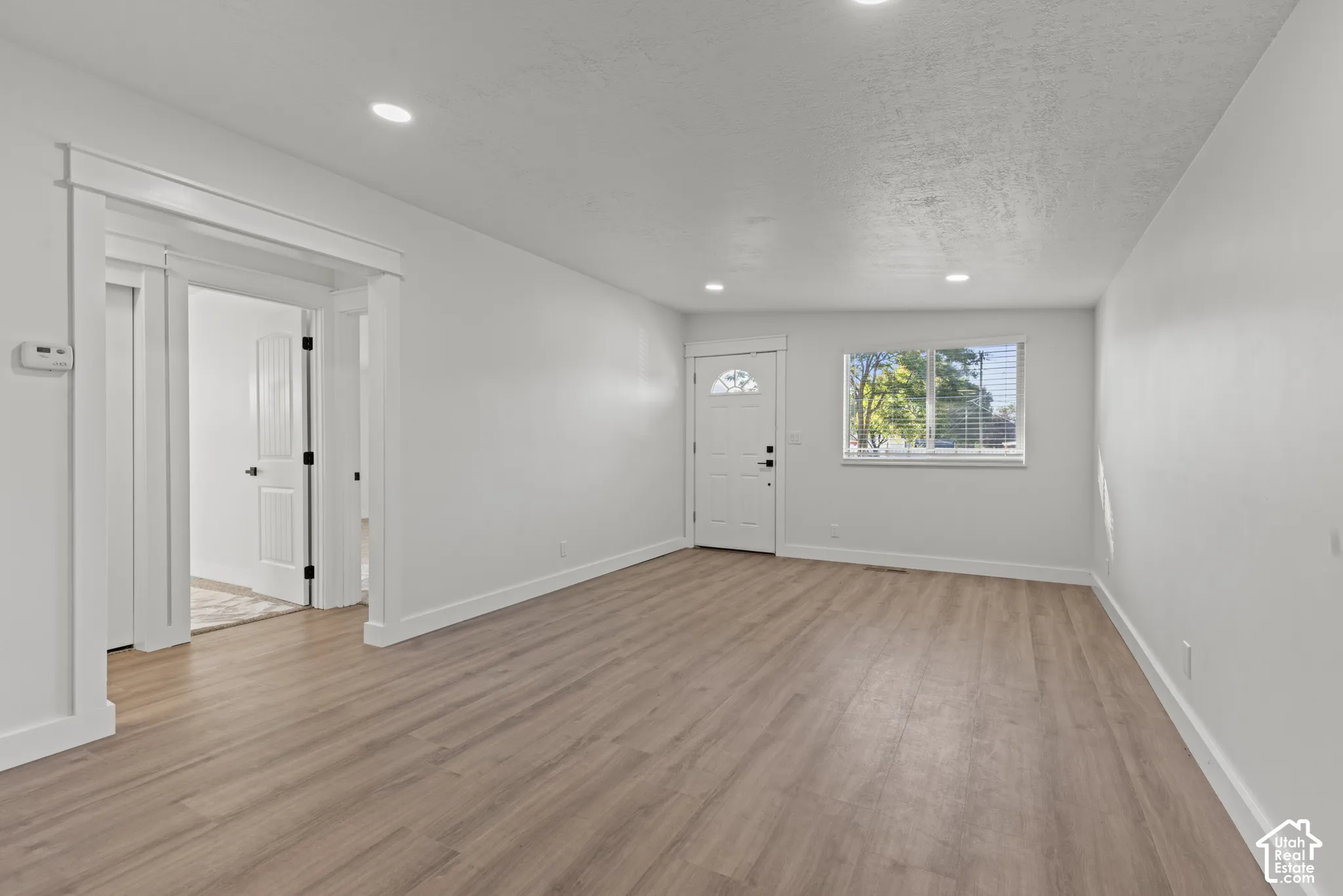 Living area featuring light wood-finish flooring, recessed lighting, neutral wall paint, white trim, and a window with horizontal blinds