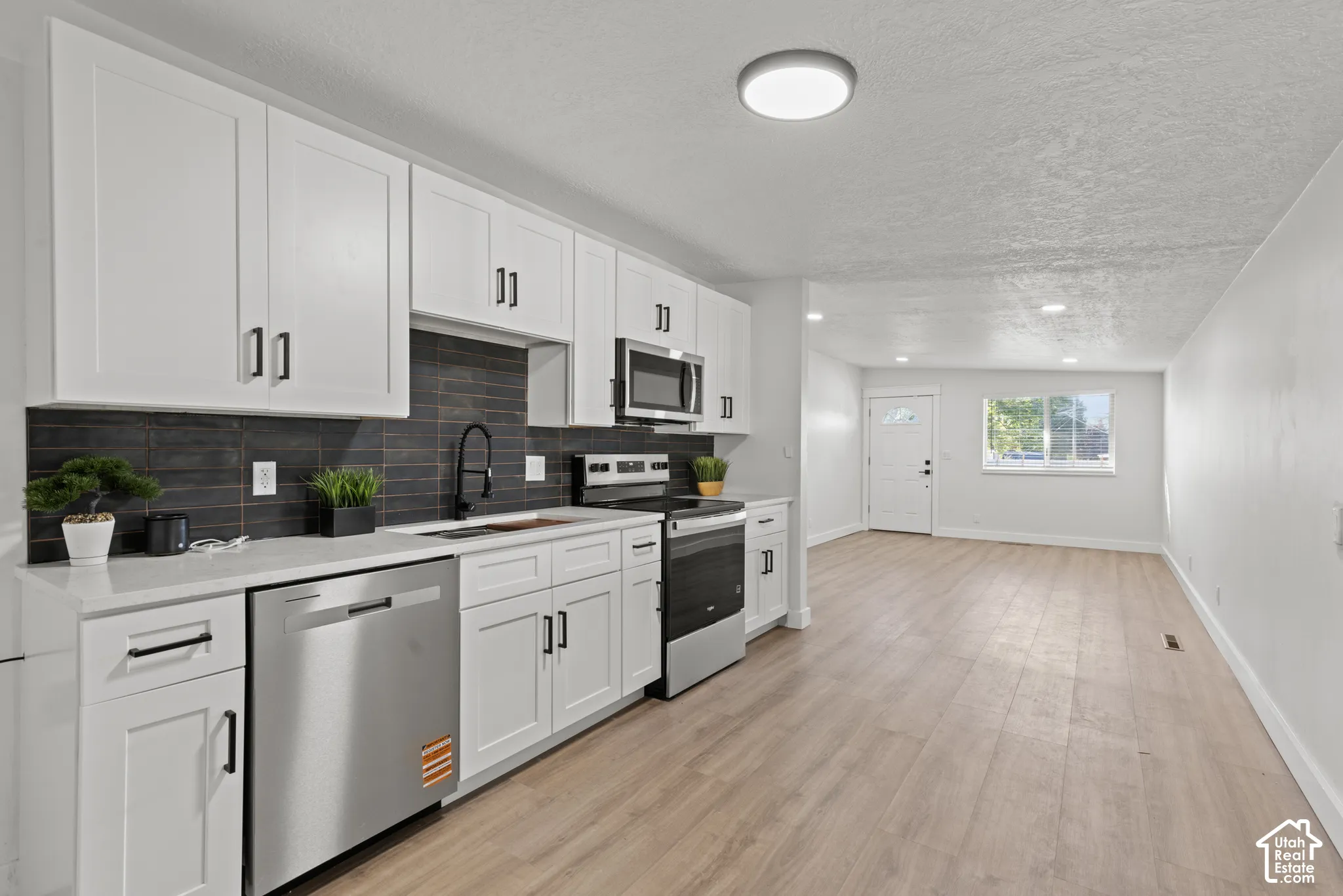 Kitchen featuring white cabinetry, quartz countertops, dark tiled backsplash, stainless steel appliances, and wood-finish flooring