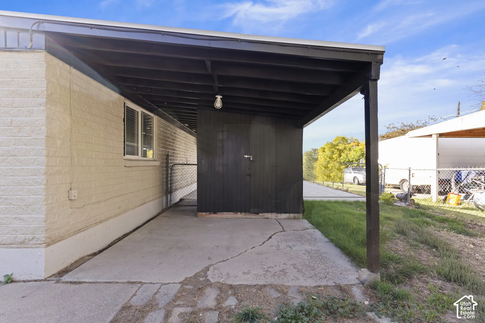 Covered carport featuring an integrated storage structure, masonry exterior walls, and a concrete pad