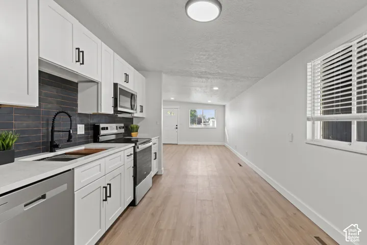 Kitchen featuring white shaker-style cabinetry, dark tiled backsplash, wood-finish flooring, quartz countertops, and stainless steel appliances