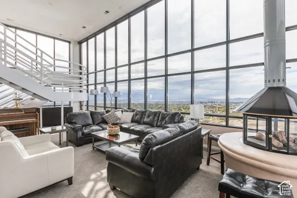 Floor-to-ceiling multi-panel windows, custom suspended metal fireplace, white metal open-tread staircase with integrated railings, and high ceilings