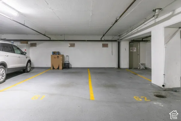 Covered parking area featuring concrete flooring, painted masonry walls, overhead fluorescent lighting, and two designated parking stalls with yellow painted markings
