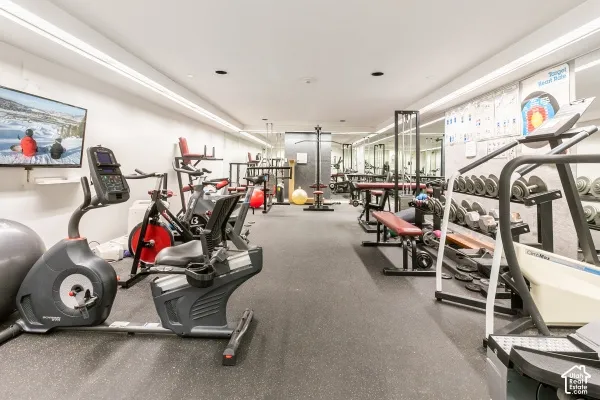 Fitness area featuring industrial-style rubberized flooring, expansive wall-to-wall mirrors, and recessed ceiling lighting