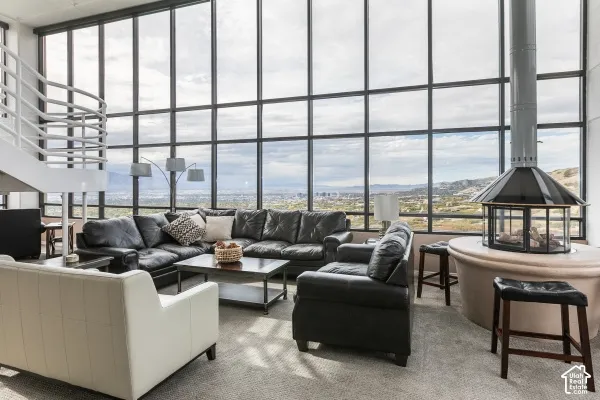 Floor-to-ceiling multi-pane windows, freestanding circular fireplace with a conical hood, open-tread staircase with metal railing, and carpeted flooring