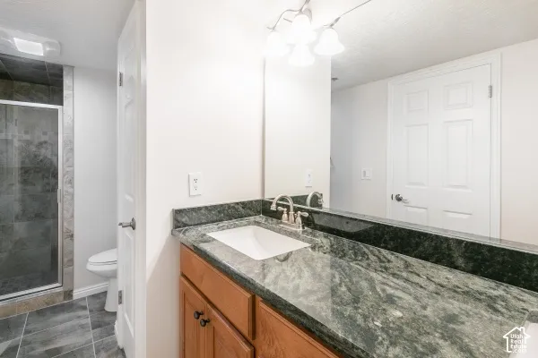 Bathroom featuring a stone countertop, wood-finish vanity cabinetry, under-mount sink, multi-bulb vanity lighting, and a glass-enclosed shower with tile flooring