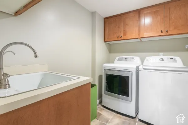 Laundry area featuring wood-finish upper cabinetry, a utility sink with a high-arc faucet, and tiled flooring