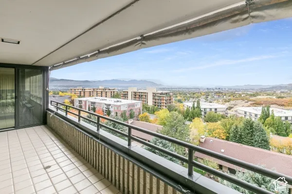 Covered balcony featuring neutral tile flooring, metal railings, and a retractable awning overlooking a panoramic mountain and urban landscape