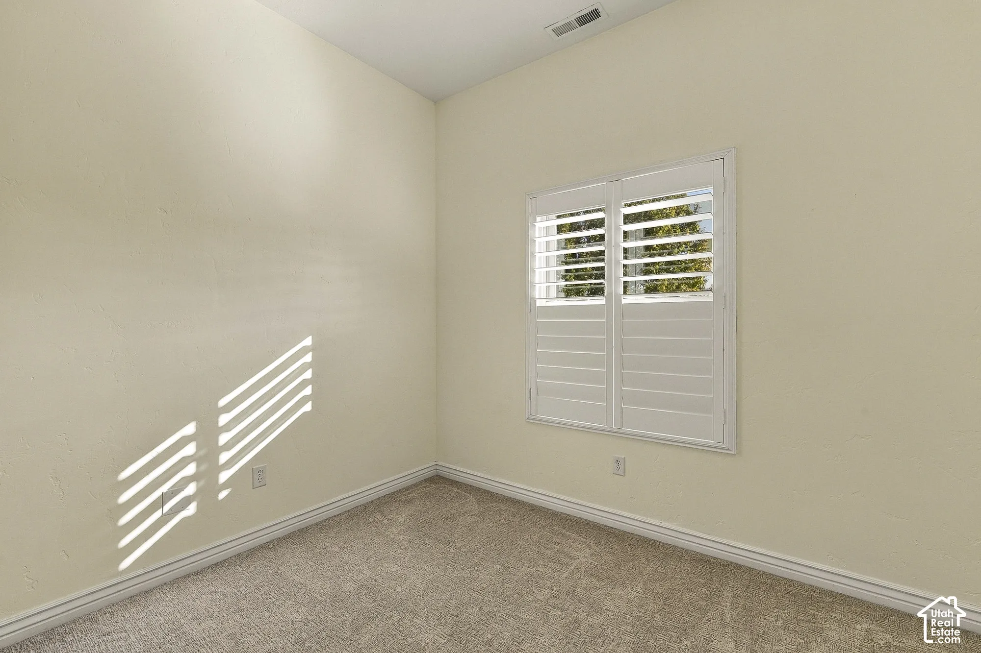Neutral wall paint, plush carpeting, and dual-panel window with installed plantation shutters