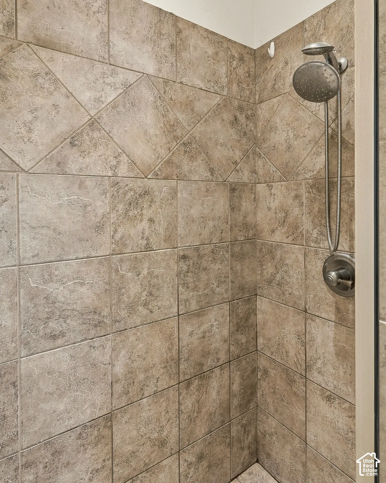 Shower enclosure featuring ceramic wall tile with an inset diamond-pattern border, polished metal handheld showerhead, and matching control valve