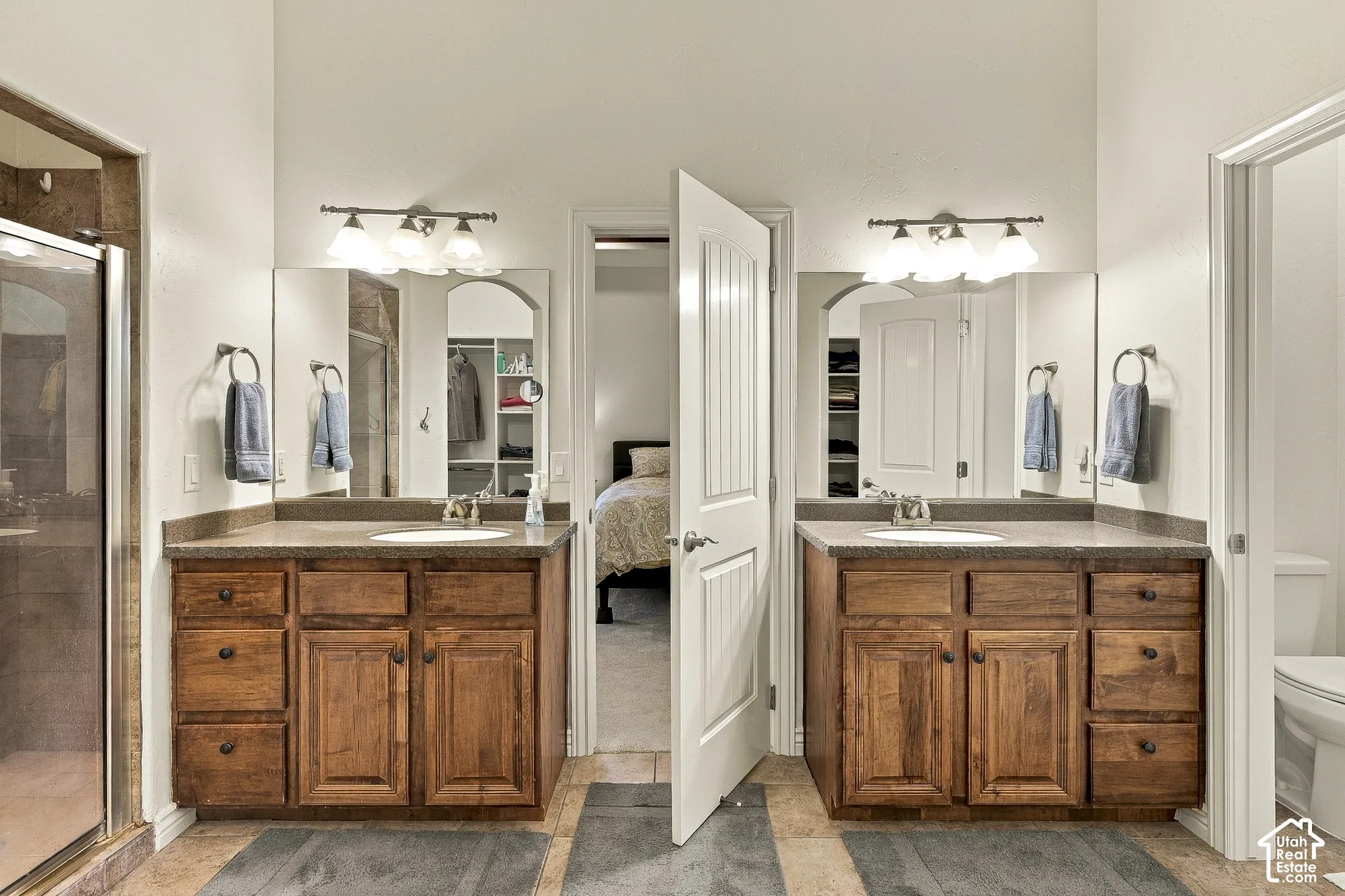 Dual wooden vanities featuring stone-surface countertops, integrated sinks, framed mirrors, and multi-light wall fixtures