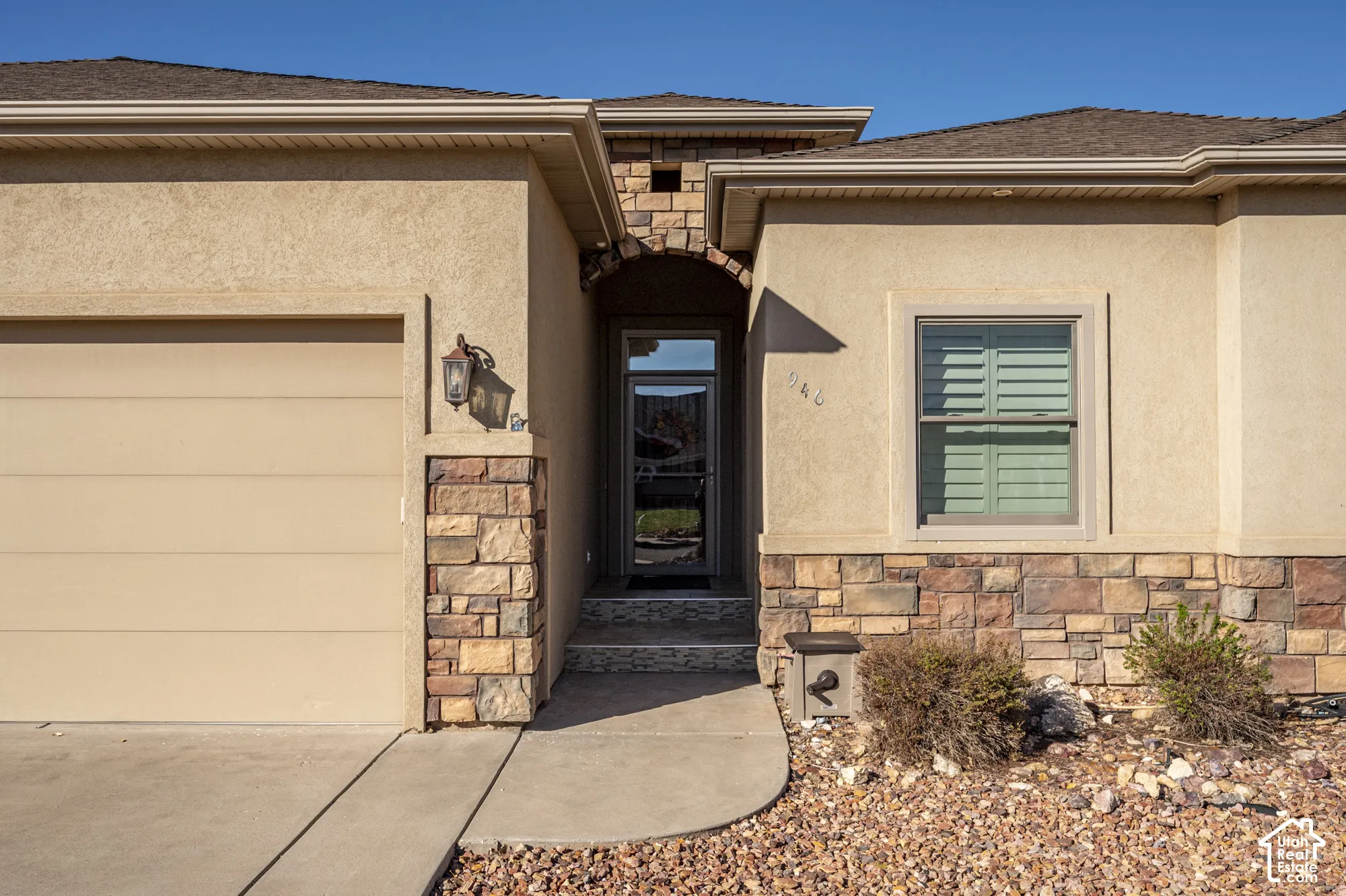 Stucco exterior featuring natural stone accents, arched entryway, and attached garage