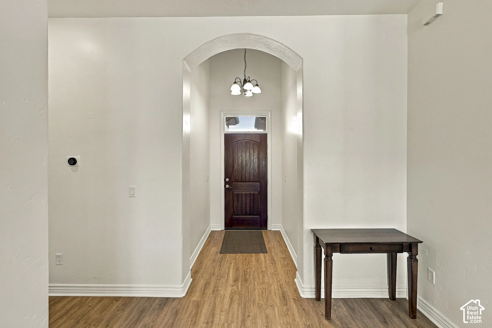 Entryway featuring an arched ceiling detail, wood-finish flooring, a dark-stained wood entry door with transom window, and a multi-light pendant fixture