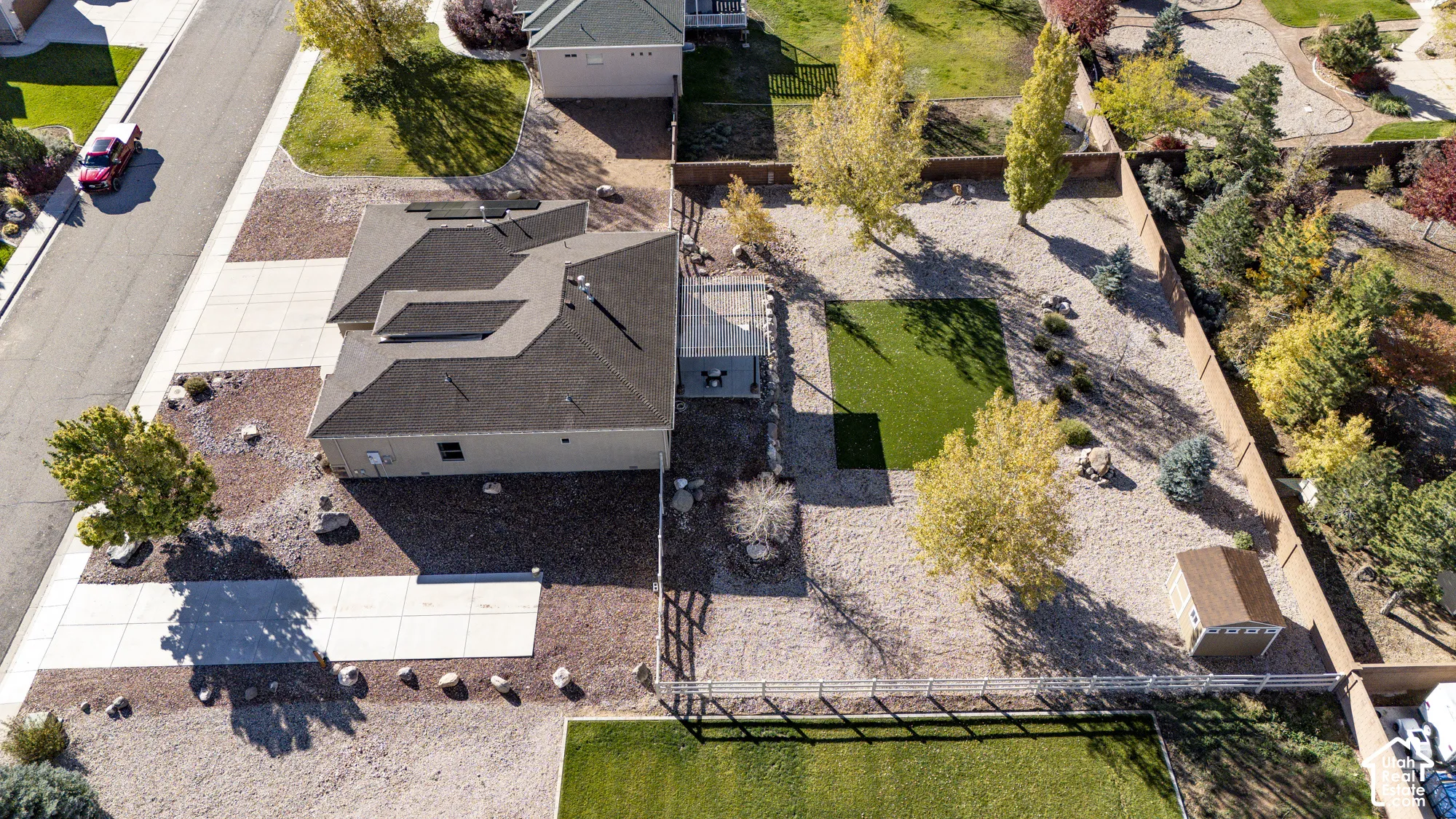Aerial view featuring a paved driveway, low-maintenance gravel landscaping, a section of artificial turf, an attached patio cover, and a detached storage structure
