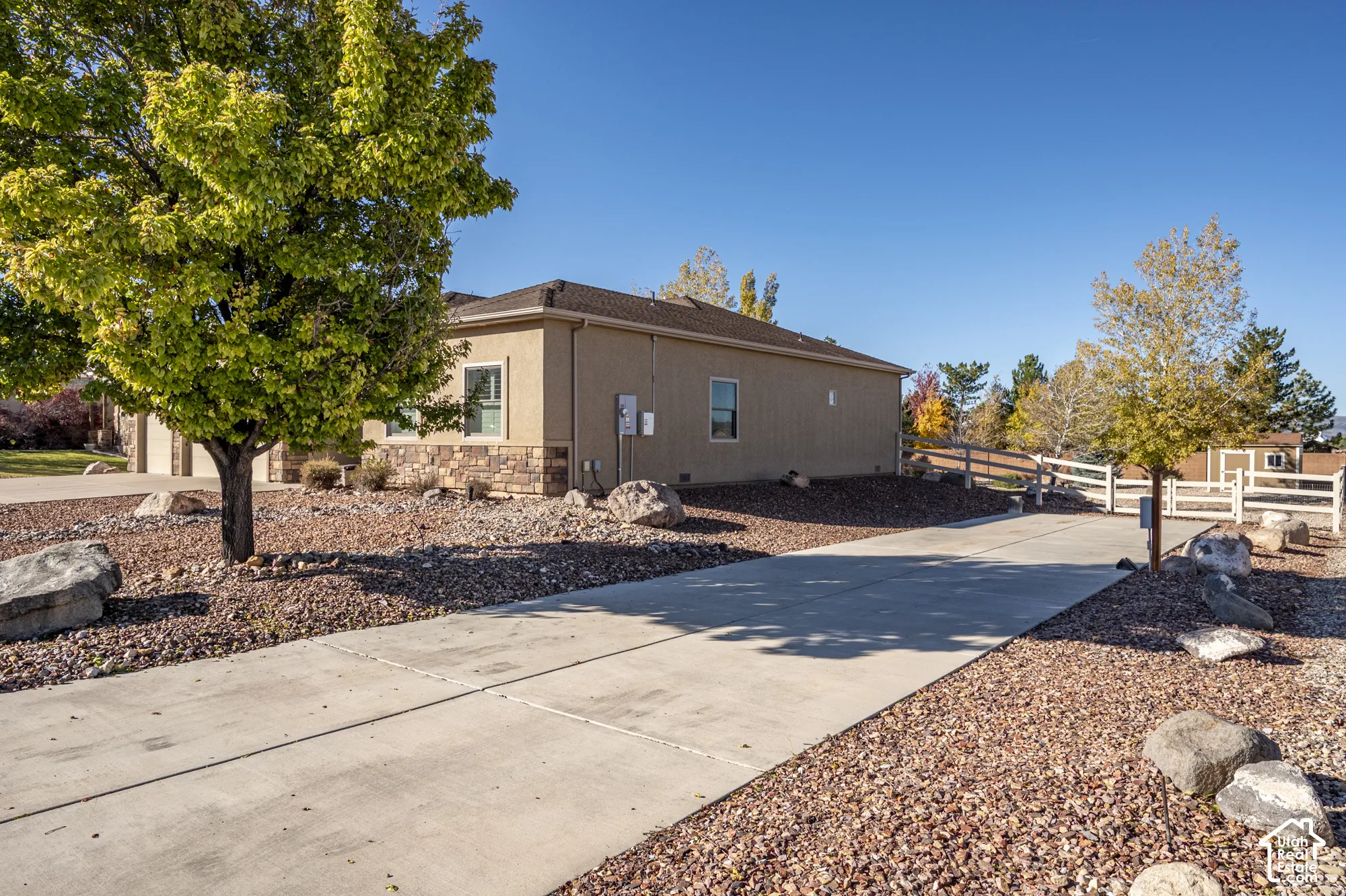 Stucco exterior with stone veneer accents, concrete driveway, and white split-rail fencing