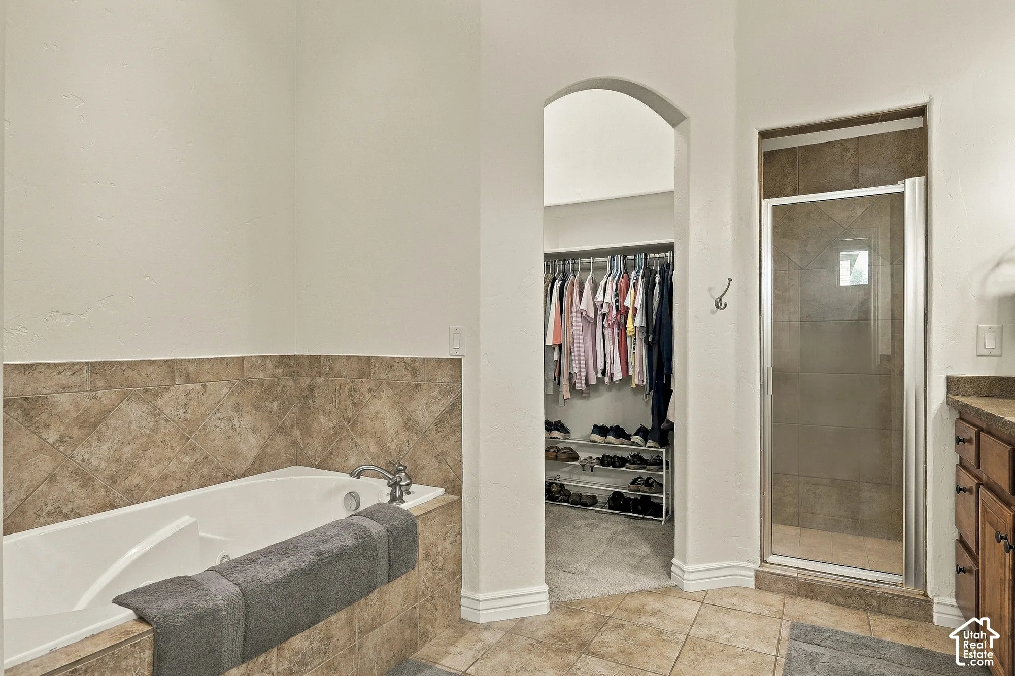 Soaking tub featuring tile surround, glass-enclosed shower, walk-in closet with built-in storage, and tile flooring