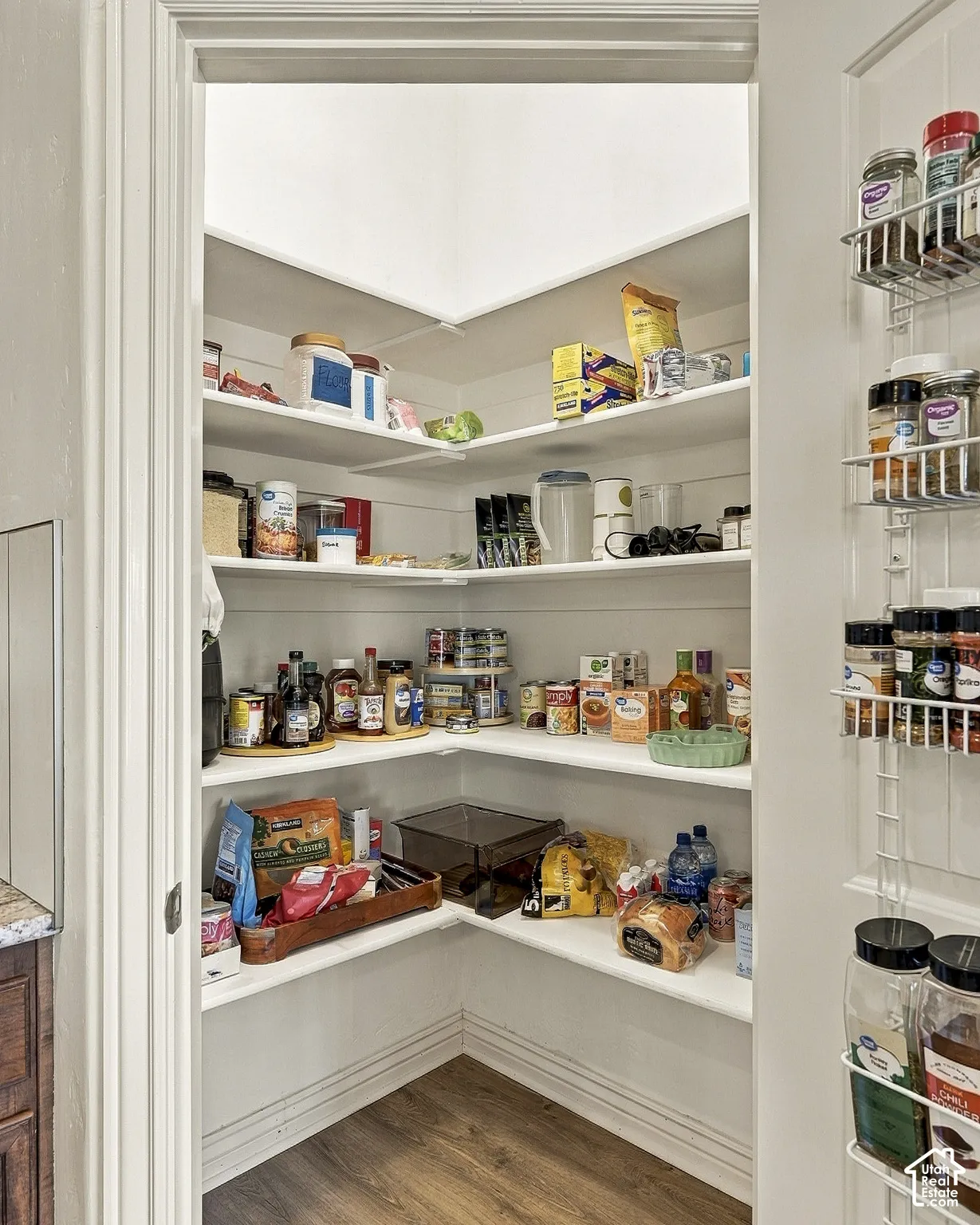 Walk-in pantry featuring white shelving, shiplap wall detailing, and wood-finish flooring with an attached door-mounted spice rack