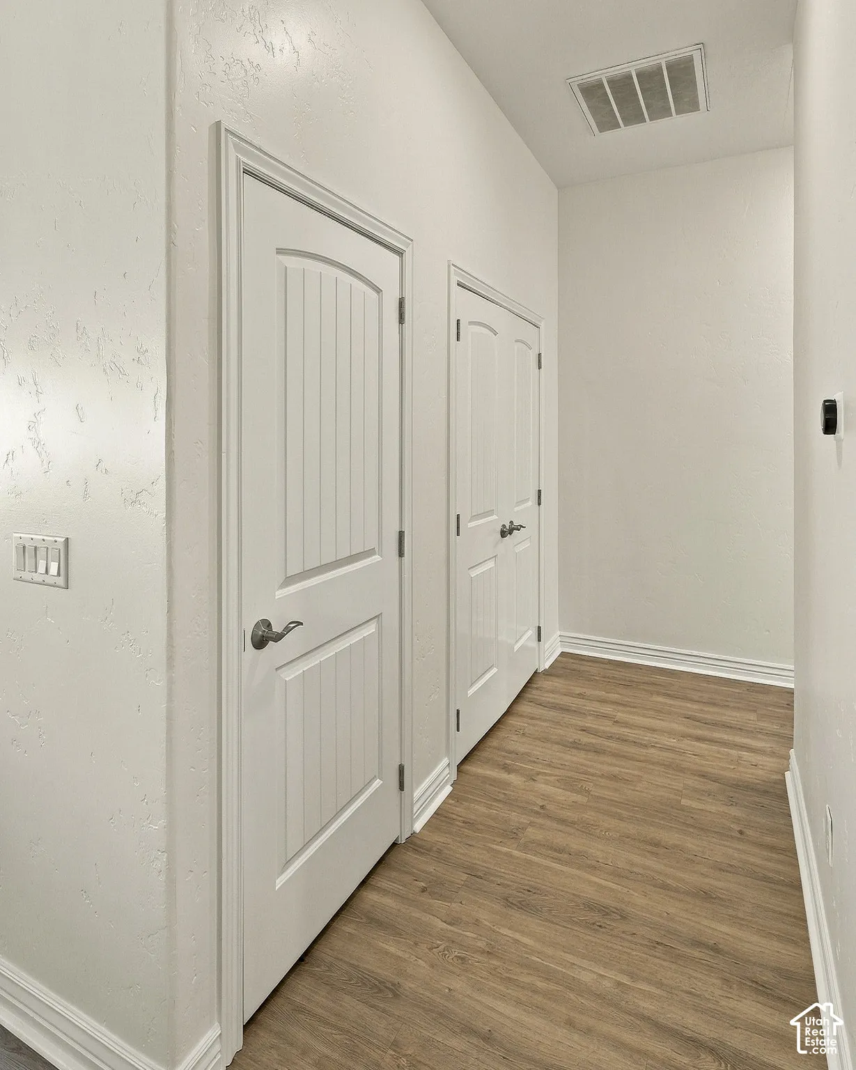 Hallway featuring wood-finish flooring, two white panel doors with satin-finish hardware, and crisp neutral wall paint