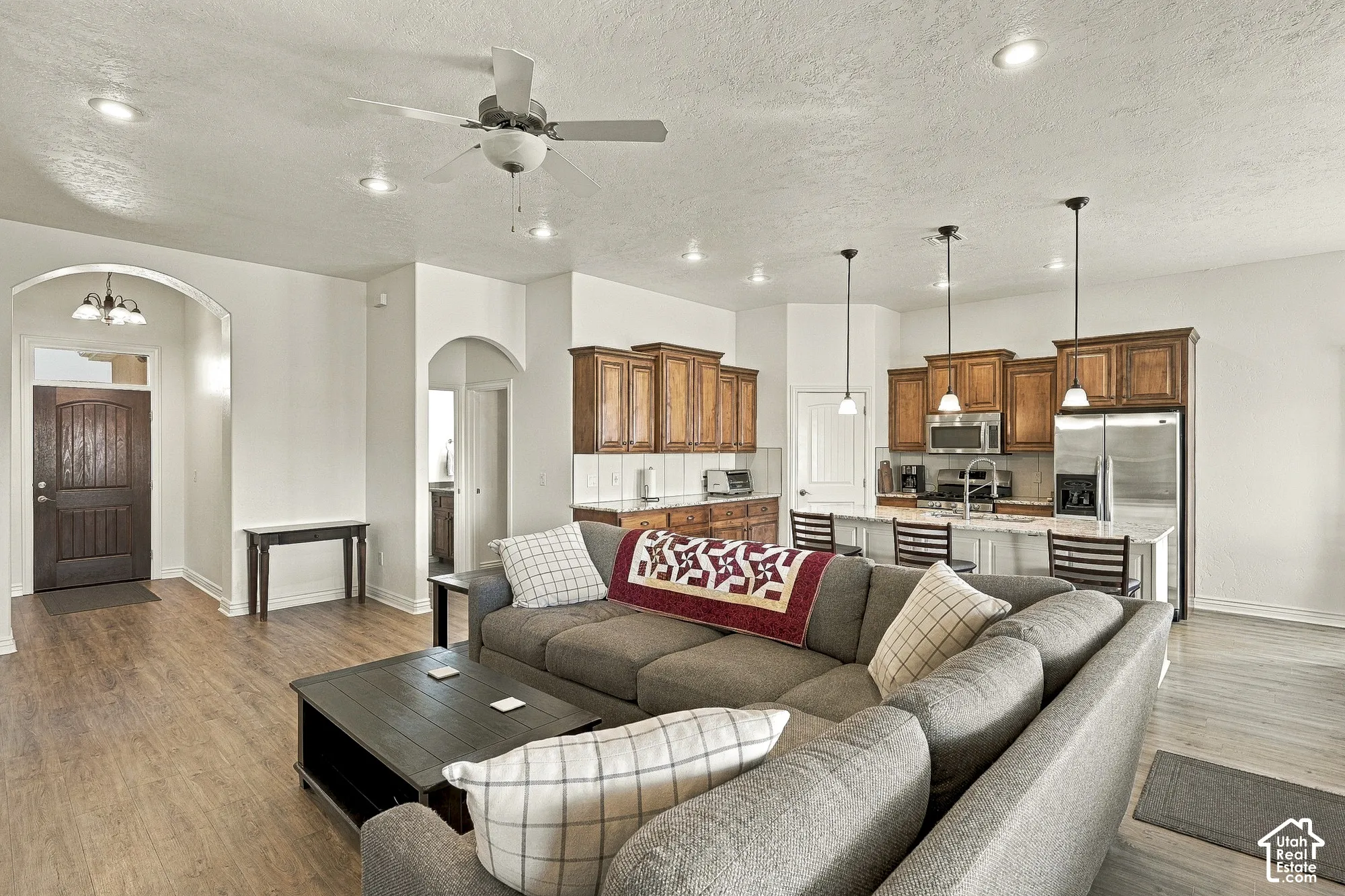Open-concept interior featuring wood-finish flooring, arched architectural detailing, recessed lighting, wood cabinetry, and a kitchen island with pendant fixtures