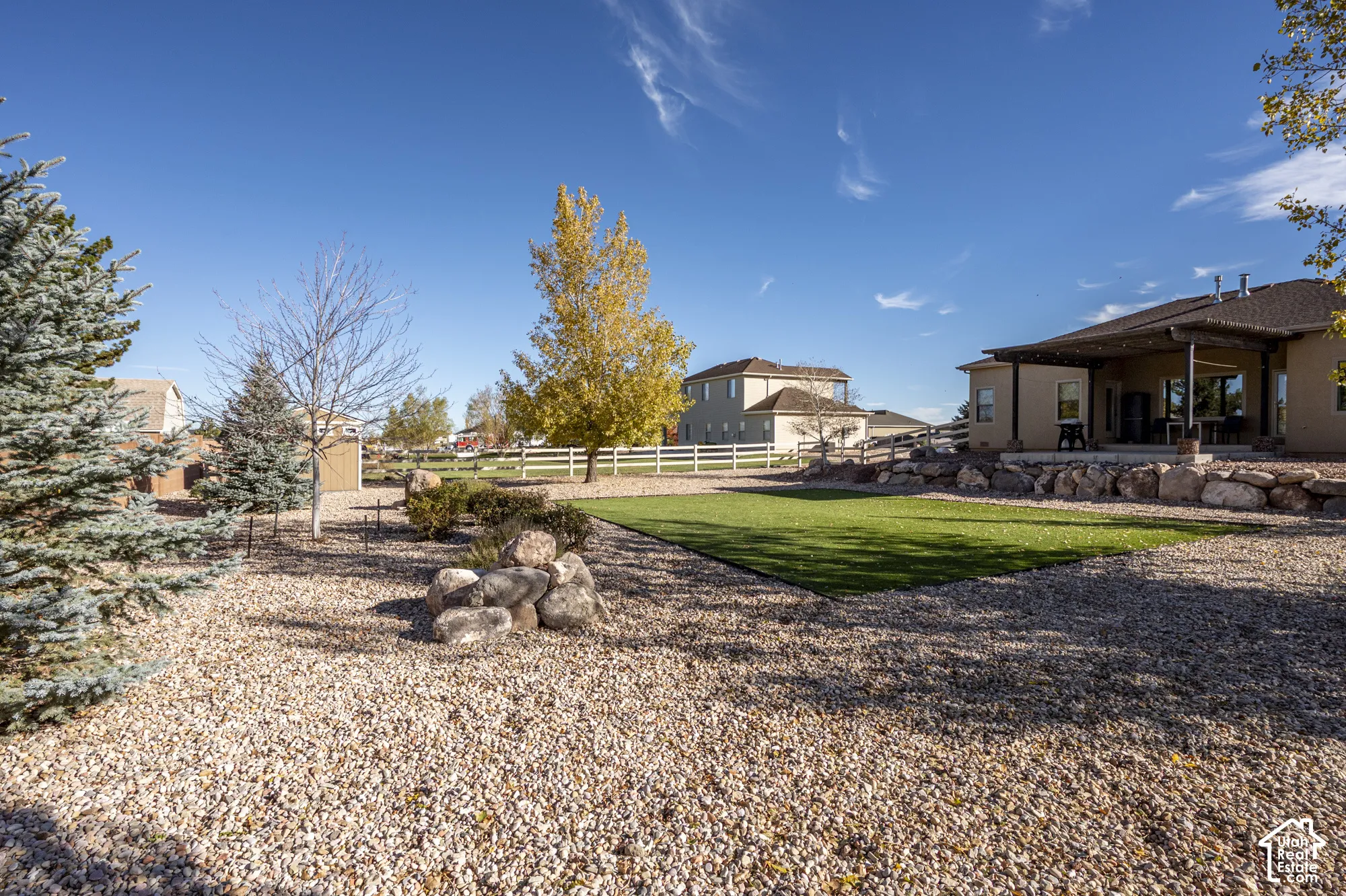 Backyard featuring synthetic turf, decorative stone landscaping, boulders, and a covered patio with a wooden pergola