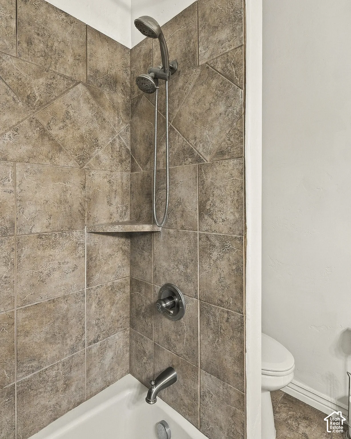 Shower enclosure featuring square-tile surround with diagonal-patterned accents, built-in corner shelf, and brushed-finish plumbing fixtures