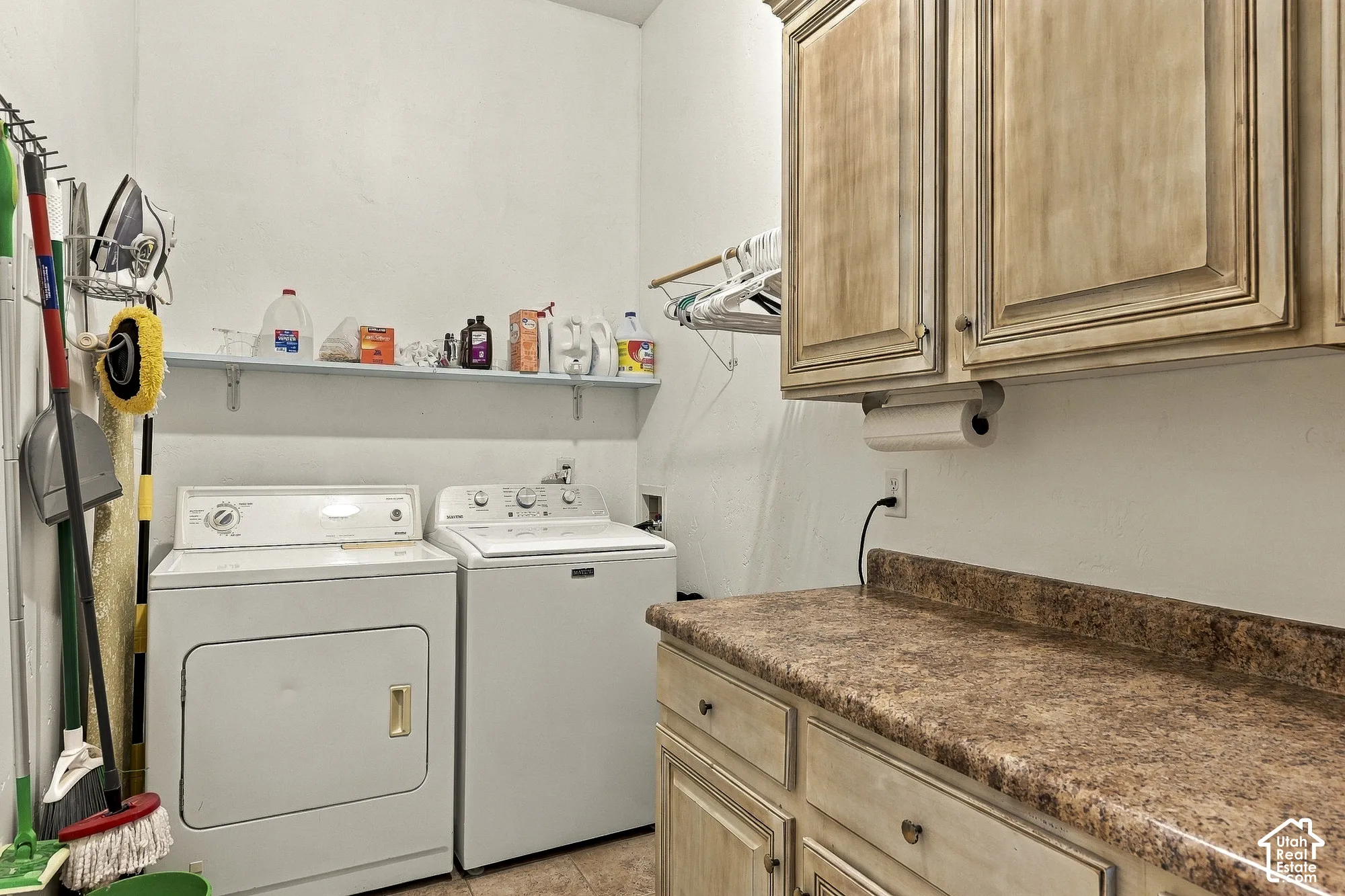Laundry area featuring stained wood-finish cabinetry, stone-texture laminate countertop, and a wall-mounted storage shelf