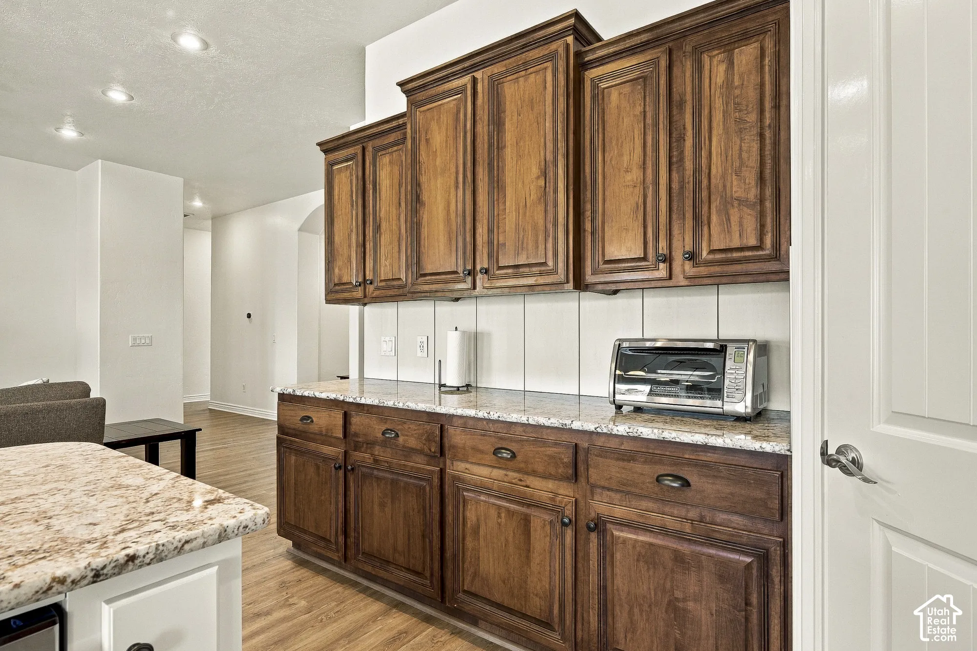 Custom cabinetry with raised-panel doors, speckled stone countertops, vertical plank backsplash, recessed ceiling lighting, and wood-finish flooring