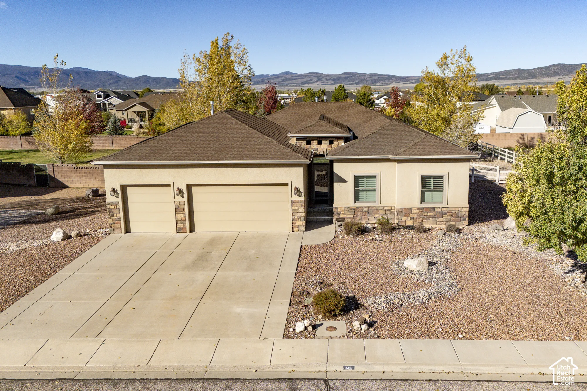 Single-story residence featuring a stucco and stone veneer exterior, an attached three-car garage, concrete driveway, and a mountain backdrop