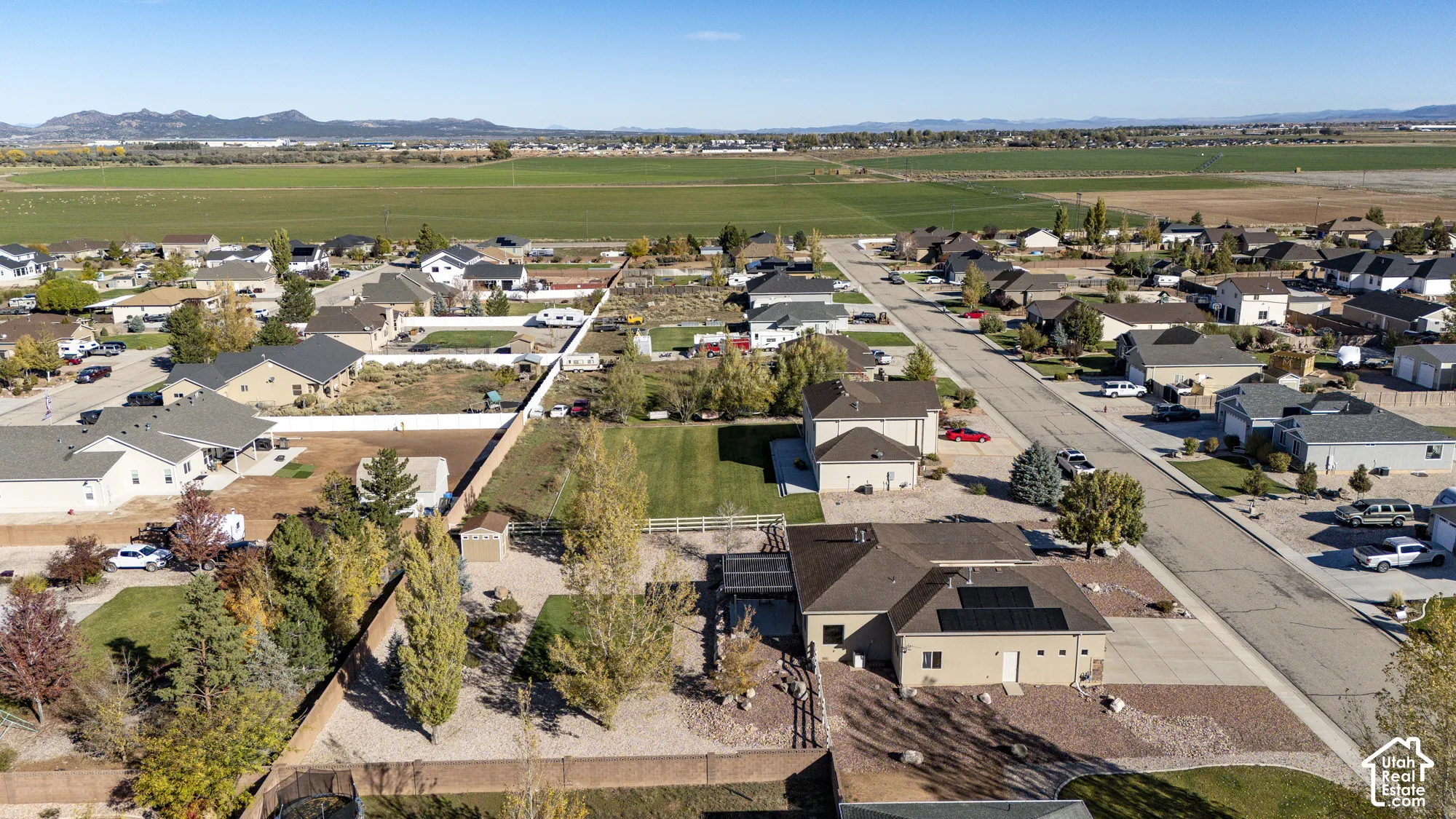 Aerial perspective showcasing a property with roof-mounted solar panels, a covered patio structure, and a fenced rear yard with mature trees