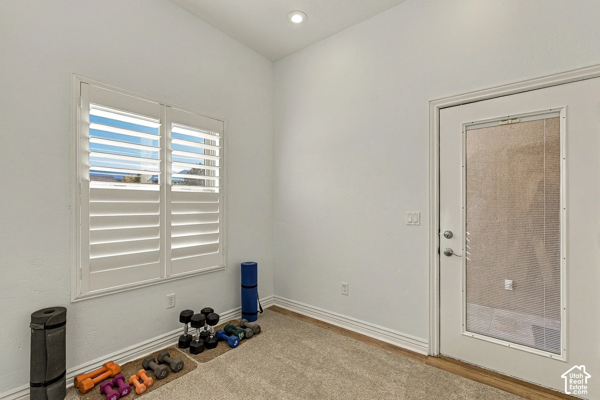High-ceiling interior space featuring white plantation shutters, neutral-tone carpeting, and an exterior door with a glass insert