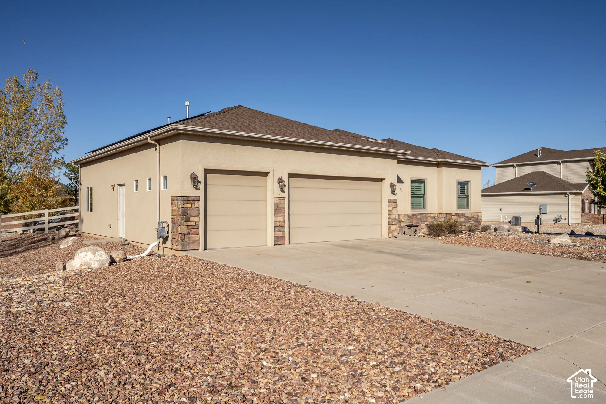 Stucco exterior featuring stone masonry accents, a three-car garage, and roof-mounted solar panels