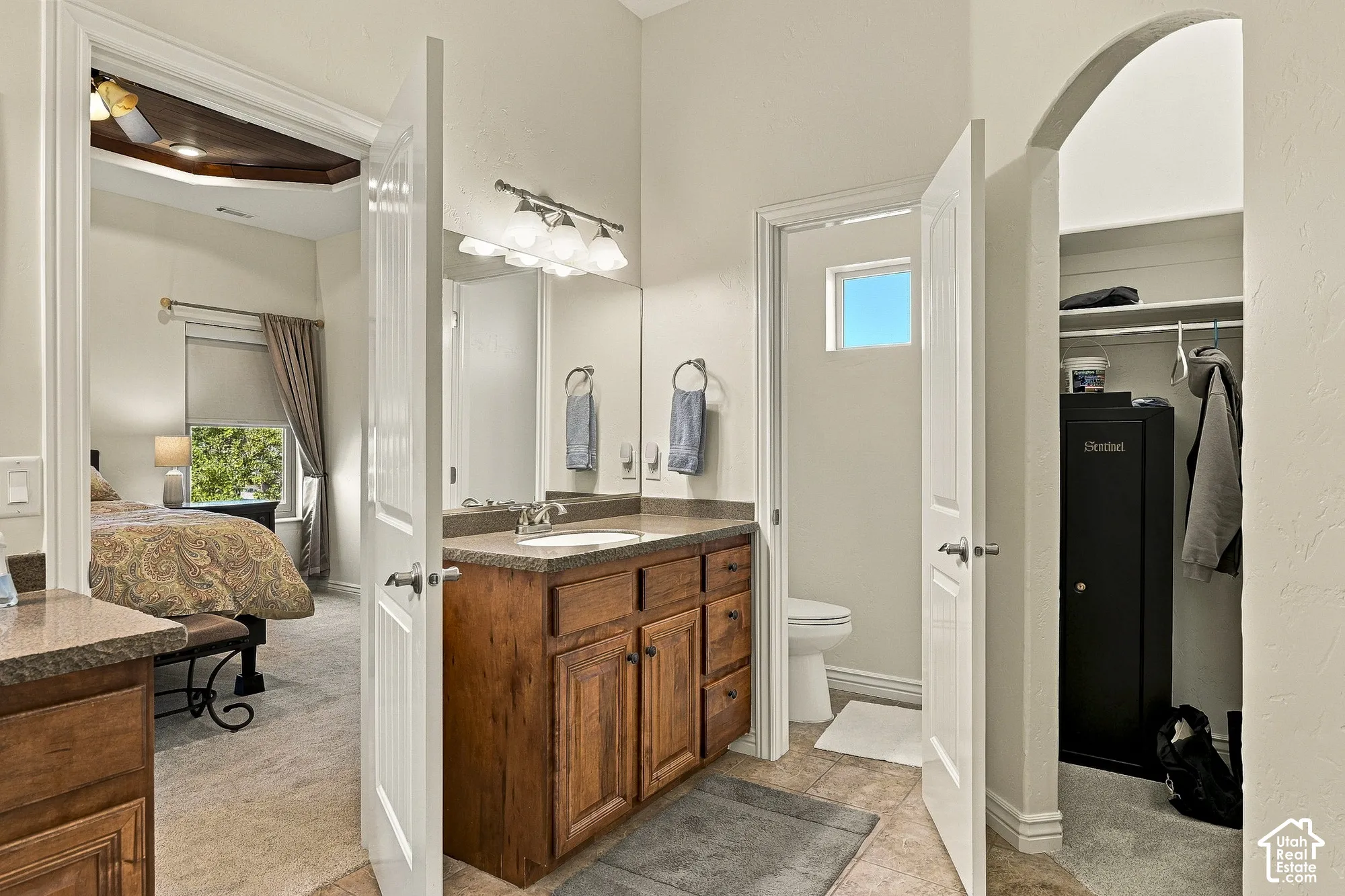 Bathroom featuring custom-stained wood cabinetry, solid-surface vanity countertop, porcelain tile flooring, and a walk-in closet with an arched entry