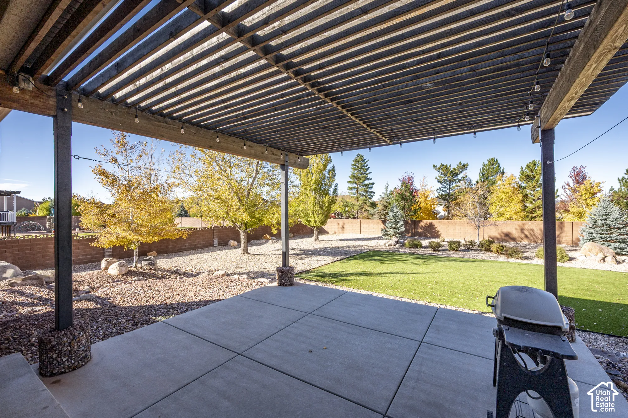 Outdoor living space featuring a concrete patio, wood-slat pergola, artificial turf, gravel landscaping, and a masonry perimeter wall