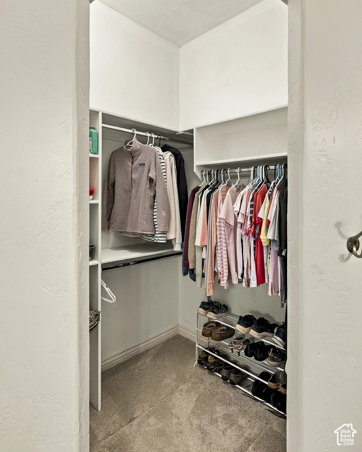 Walk-in closet featuring white built-in shelving, dual-tier clothing rods, and wall-mounted metal hooks