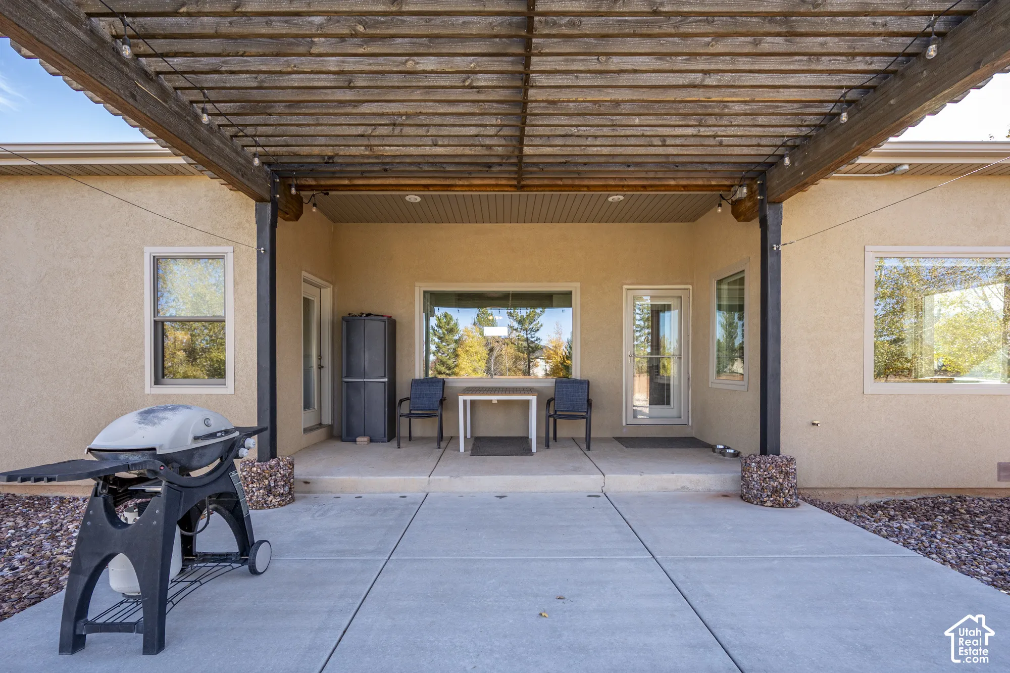 Covered concrete patio featuring a timber pergola, recessed lighting, and stone-accented support columns