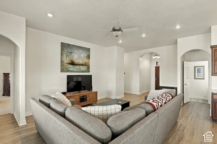 Interior space featuring wood-finish flooring, recessed lighting, a central ceiling fan, and arched architectural entryways