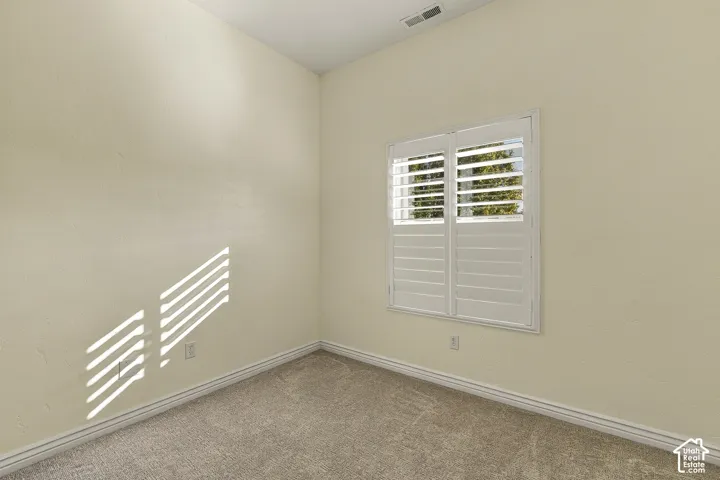 Neutral wall paint, plush carpeting, and dual-panel window with installed plantation shutters