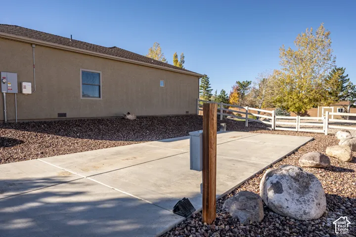 Concrete pad exterior space featuring a split-rail fence, rock landscaping, and decorative boulders