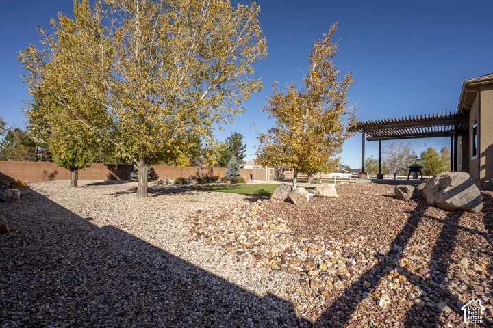 Expansive backyard featuring xeriscaped rock landscaping, mature trees, a masonry perimeter wall, and a covered pergola