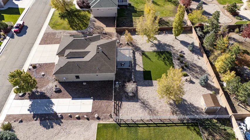 Aerial view featuring a paved driveway, low-maintenance gravel landscaping, a section of artificial turf, an attached patio cover, and a detached storage structure