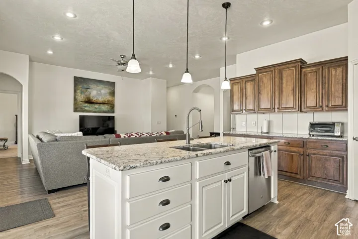 Kitchen featuring an island with a dual-basin sink, stone countertops, stained-wood cabinetry, recessed lighting, and pendant lights