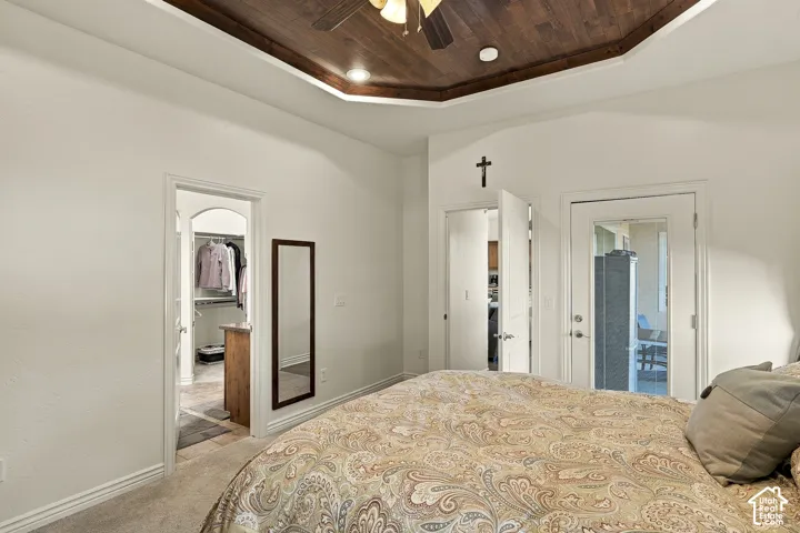 Tray ceiling with dark wood-finish plank detailing, integrated ceiling fan, recessed lighting, and glass-panel door