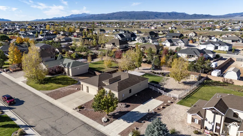 Aerial perspective of a single-story residence featuring a paved driveway, attached garage, fenced rear grounds, and mountain scenery