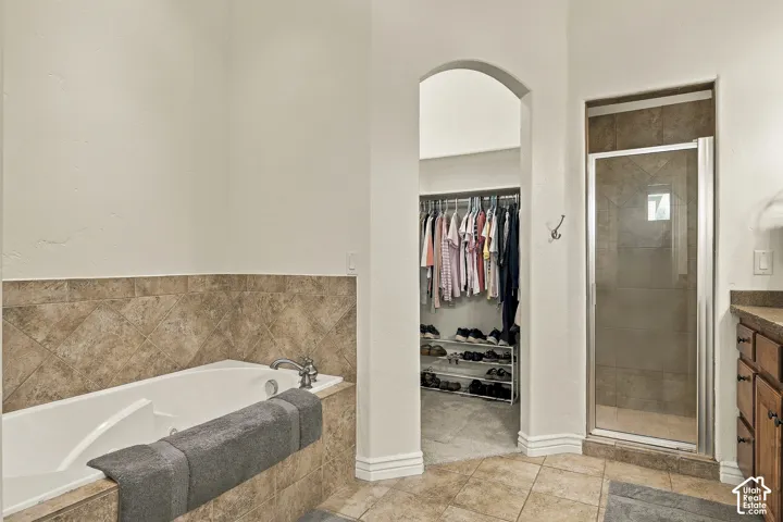 Soaking tub featuring tile surround, glass-enclosed shower, walk-in closet with built-in storage, and tile flooring
