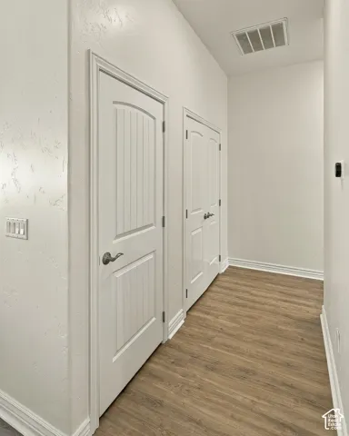 Hallway featuring wood-finish flooring, two white panel doors with satin-finish hardware, and crisp neutral wall paint