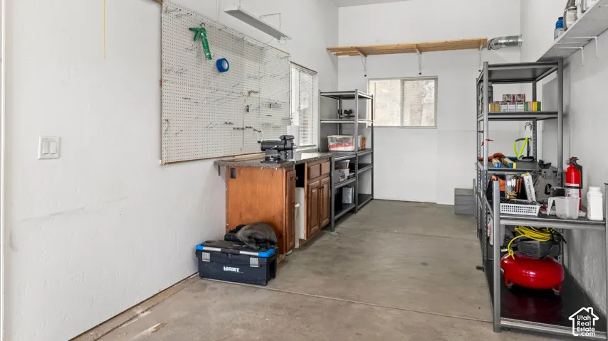 Workshop area featuring built-in wood cabinetry, a durable countertop, wall-mounted pegboard, dual sliding windows, and open shelving