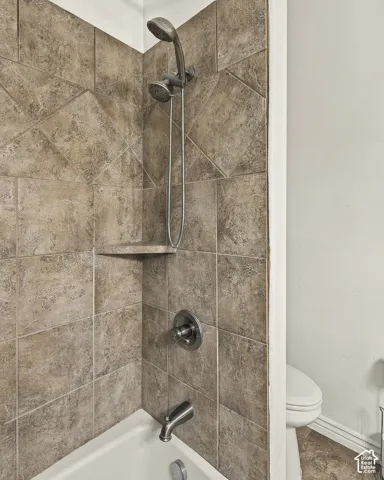 Shower enclosure featuring square-tile surround with diagonal-patterned accents, built-in corner shelf, and brushed-finish plumbing fixtures