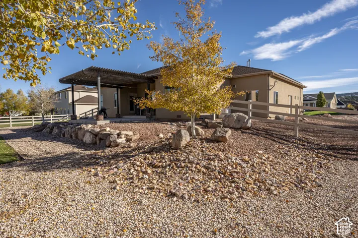 Exterior featuring a covered pergola, stacked rock retaining wall, white rail fencing, and stone landscape ground cover