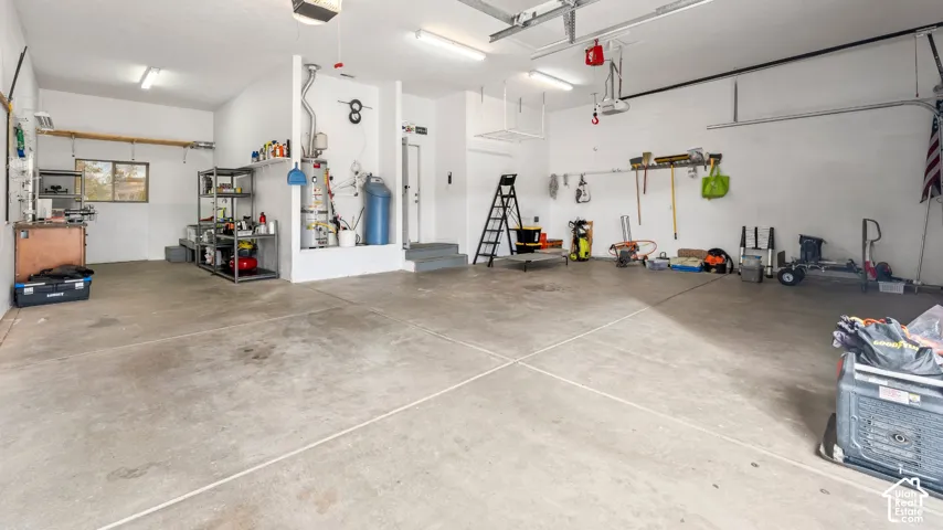 Spacious multi-car garage featuring a concrete floor, built-in shelving, overhead lighting, and an attached water heater