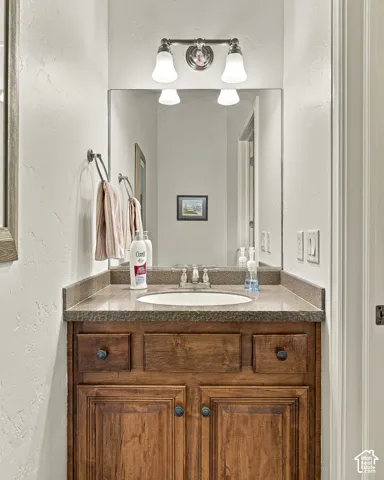Vanity featuring a stone-composite countertop with an integrated oval sink, natural wood cabinetry, a large rectangular mirror, and dual-light wall-mounted fixture